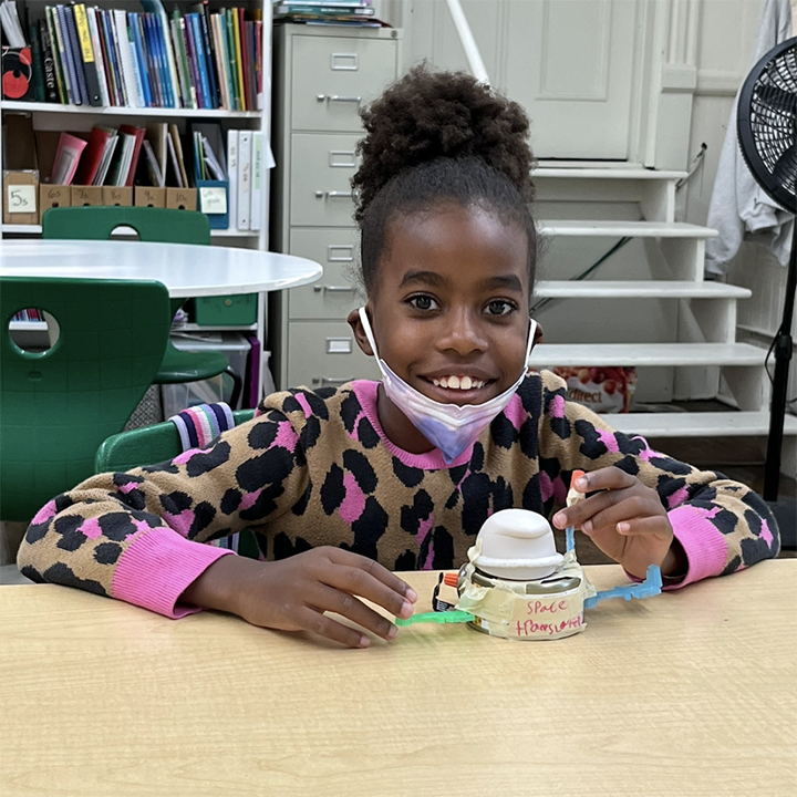 A girl smiles with her spaceship prototype, created with recyclables.