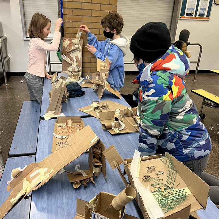 Kids work together to create large structures with cardboard that include simple are more complex mechanisms/ machines.